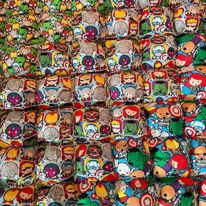 May include: A collection of square fabric items, each featuring a different Marvel superhero character. The fabric has a colorful cartoon style with characters like Captain America, Iron Man, and Hulk. The items are arranged in a grid pattern.