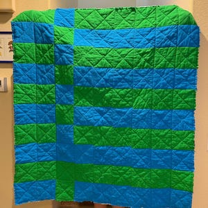 May include: A handmade quilt with a geometric pattern of alternating blue and green squares and horizontal stripes. The quilt is quilted with a diamond pattern and has a raw edge.