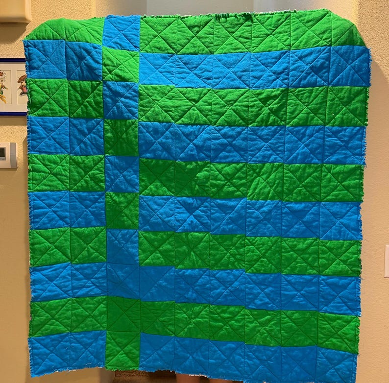 May include: A handmade quilt with a geometric pattern of alternating blue and green squares and horizontal stripes. The quilt is quilted with a diamond pattern and has a raw edge.