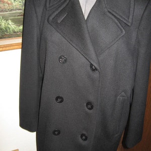 May include: A black double-breasted peacoat with six buttons. The coat has a large collar and is made of a thick, warm fabric.