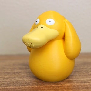 May include: A yellow duck-like Pokemon figurine with a large beak and small eyes. The figurine is made of a smooth, matte plastic.