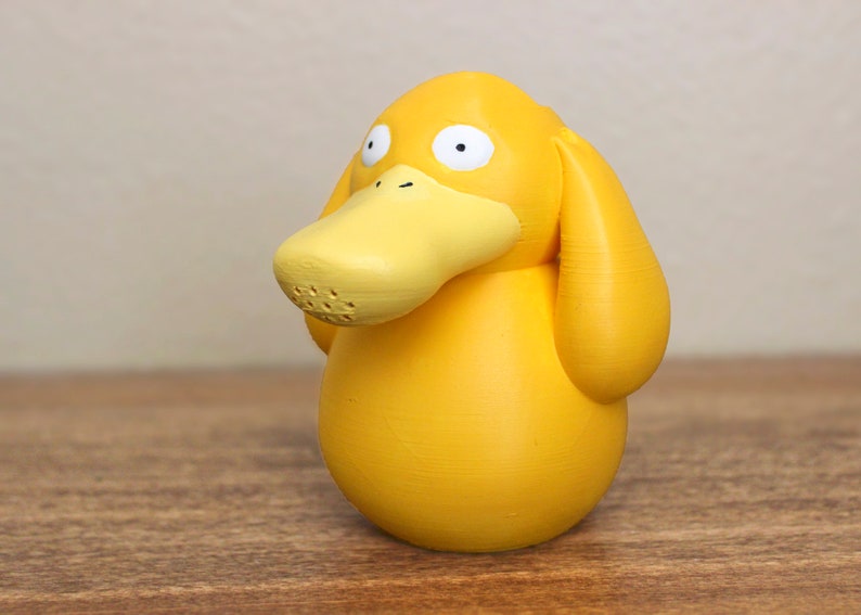 May include: A yellow duck-like Pokemon figurine with a large beak and small eyes. The figurine is made of a smooth, matte plastic.