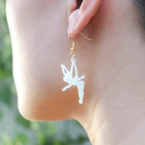 May include: A pair of gold dangle earrings with a white silhouette of a fairy with wings outstretched.
