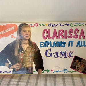May include: A vintage Clarissa Explains It All board game box. The box features a photo of the show's star, the Nickelodeon logo, and the game's title in pink and blue. The box is decorated with colorful doodles.
