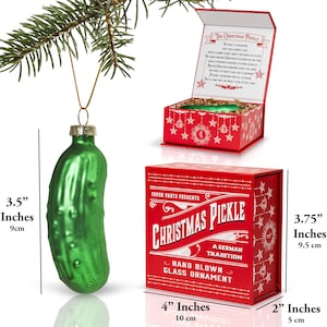 May include: A green glass Christmas pickle ornament in a red box with white lettering that reads "Favor Parts Presents Christmas Pickle A German Tradition Hand Blown Glass Ornament". The ornament is 9 cm tall and the box is 10 cm wide and 5 cm tall.