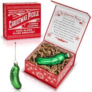 May include: A green glass pickle ornament in a red box with a white background. The box has a poem about the Christmas pickle tradition. The ornament is hand-blown and comes with a string for hanging.