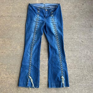 May include: Blue denim jeans with white stitching and black lacing down the sides of the legs.