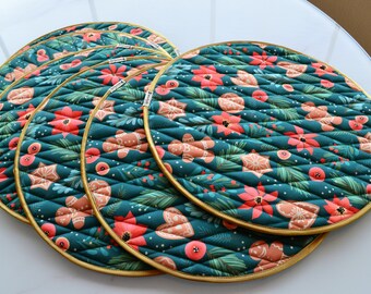 May include: Set of six teal blue quilted round placemats with a gold trim. The placemats feature a repeating pattern of red poinsettias, gingerbread cookies, and green leaves.