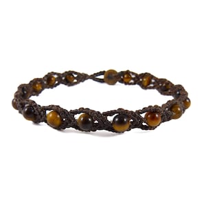May include: A brown macrame bracelet featuring tiger eye beads. The bracelet is made of dark brown cord, with the beads evenly spaced around the circumference. The tiger eye beads have a warm, golden-brown color.