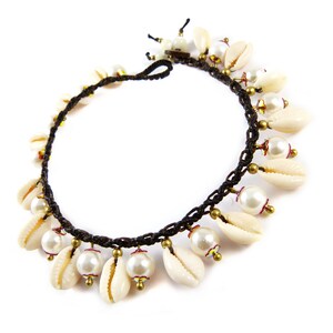Könnte beinhalten: Ein braunes Kordelarmband mit weißen Muschel- und Perlenperlen. Das Armband ist mit einem Knoten gebunden und hat einen kleinen Metallverschluss.