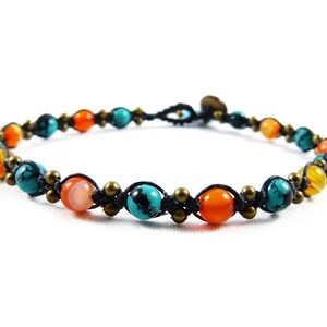 Puede incluir: Una pulsera de cuentas con cuentas turquesas, naranjas y amarillas. Las cuentas están ensartadas en un cordón negro y acentuadas con pequeñas cuentas de color latón. La pulsera está diseñada para ser usada alrededor de la muñeca.