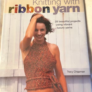 May include: A book titled "Knitting with Ribbon Yarn" with a woman wearing a knitted halter top. The book cover features the title in large letters and the author's name. The top is orange and brown.