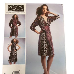 Op de afbeelding: Een Vogue Patterns naaipatroon van Koos Van Den Akker. De afbeelding toont een vrouw in een jurk met bloemenprint en een wikkelriem. Het patroon is V1301, maat Xsm-Sml-Med. Er zijn meerdere ontwerpopties.