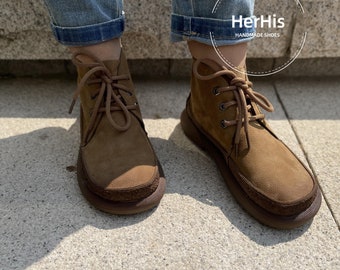 Op de afbeelding: Bruine suède enkellaarsjes met veters en een bruine rubberen zool. De laarzen worden gedragen door iemand die een blauwe jeans draagt. De tekst "HerHis HANDMADE SHOES" is zichtbaar op de afbeelding.