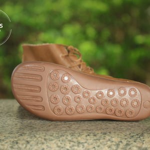 May include: Close-up of the brown leather sole of a brown leather boot. The sole has a textured pattern of small circles.