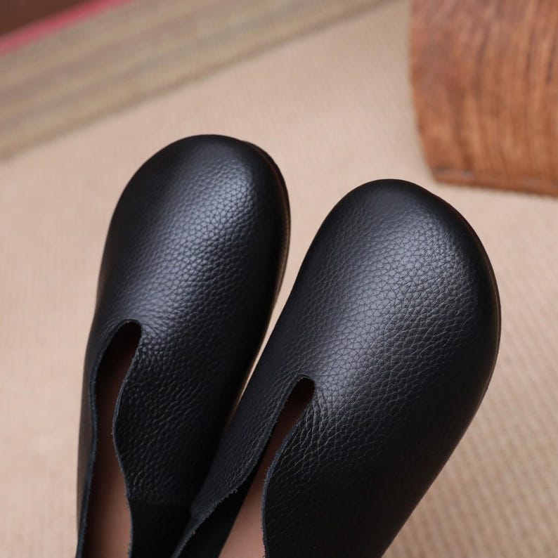 Op de afbeelding: Close-up van twee zwarte leren loafers. De schoenen hebben een ronde neus en een kleine spleet aan de bovenkant van de voet. Het leer heeft een getextureerde nerf. De schoenen zijn geschikt voor dagelijks gebruik.
