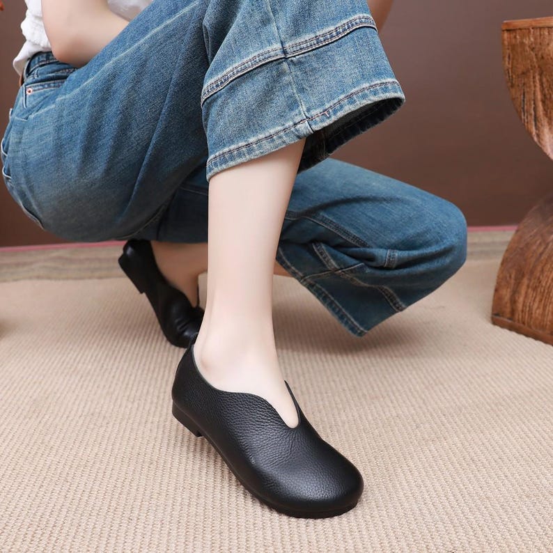 Op de afbeelding: Zwarte leren ballerina's met een ronde neus en een uniek, geschulpt vamp-ontwerp. De schoenen hebben een lage hak en een getextureerde lederen afwerking, wat een klassieke en veelzijdige stijl biedt. Deze ballerina's zijn geschikt voor dagelijks gebruik.