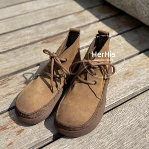 May include: A pair of brown leather ankle boots with laces. The boots have a rounded toe and a slightly raised heel. The text "HerHis Handmade Shoes" is visible on the right boot.