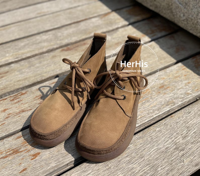 May include: A pair of brown leather ankle boots with laces. The boots have a rounded toe and a slightly raised heel. The text "HerHis Handmade Shoes" is visible on the right boot.