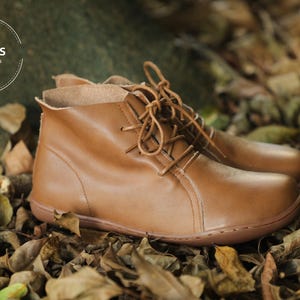 May include: A pair of brown leather ankle boots with laces. The boots are sitting on a bed of brown leaves.