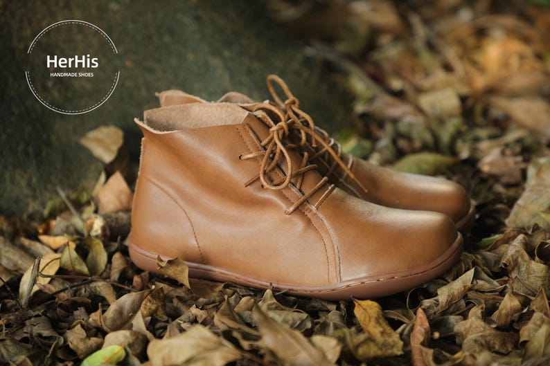 May include: A pair of brown leather ankle boots with laces. The boots are sitting on a bed of brown leaves.