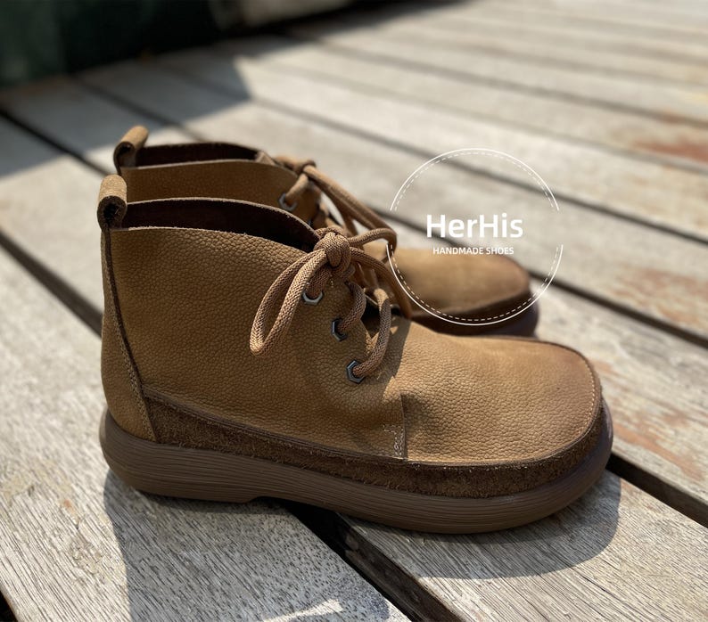 May include: A pair of brown leather ankle boots with laces. The boots have a suede-like texture and a thick sole. The brand name "HerHis Handmade Shoes" is visible on the label.