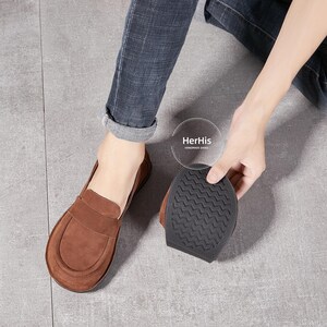 May include: Brown leather loafers with a suede finish and a black rubber sole. The sole has a textured pattern. The shoes are handmade by HerHis.