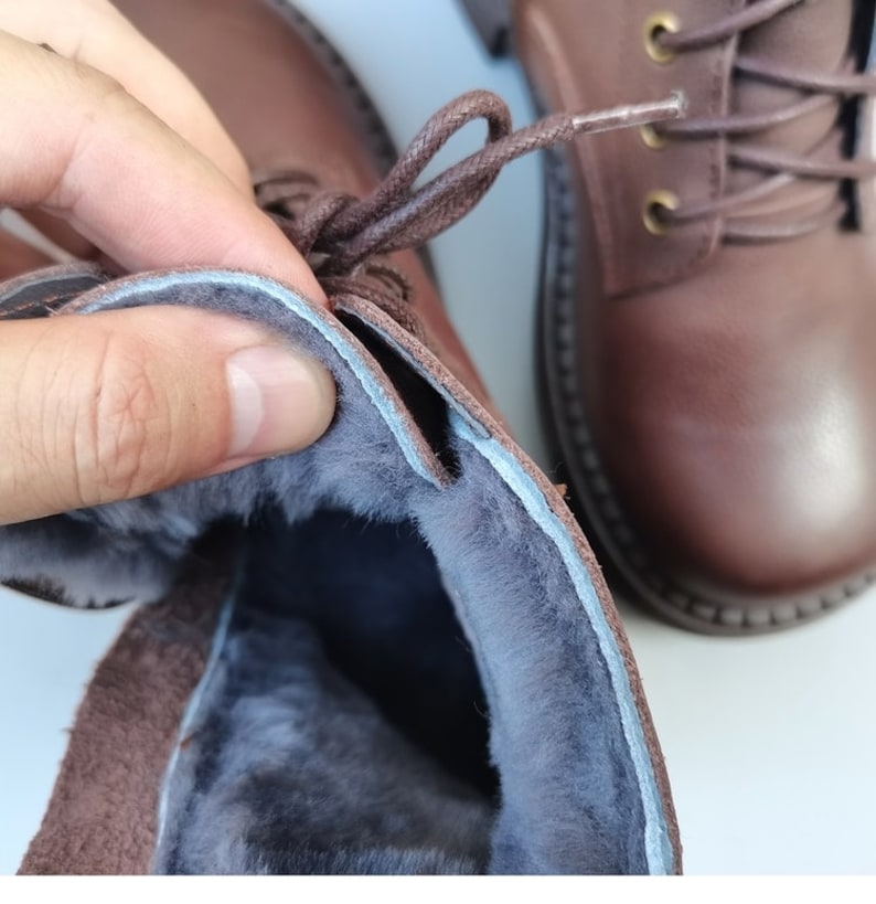 May include: Close-up of the inside of a brown leather boot with a soft, gray fleece lining. The boot has a lace-up closure.