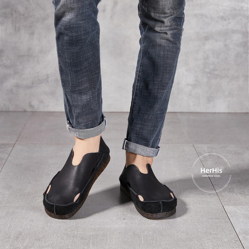 May include: A pair of black leather slip-on shoes with a simple design. The shoes have a pointed toe and a low heel. The shoes are being worn by a person wearing blue jeans.