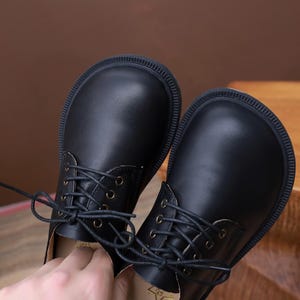 Puede incluir: Un par de zapatos negros de cuero con cordones, punta redonda y suela gruesa.