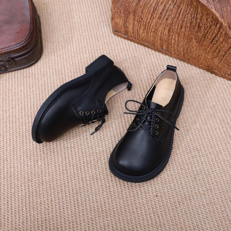 Puede incluir: Un par de zapatos negros de cuero con cordones, punta redonda y suela gruesa.
