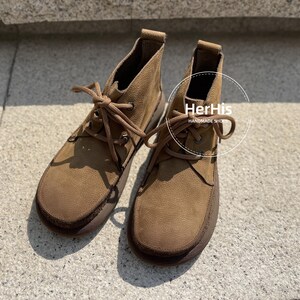 May include: A pair of brown suede ankle boots with laces. The boots have a rounded toe and a thick sole. The text "HerHis Handmade Shoes" is visible on the right boot.