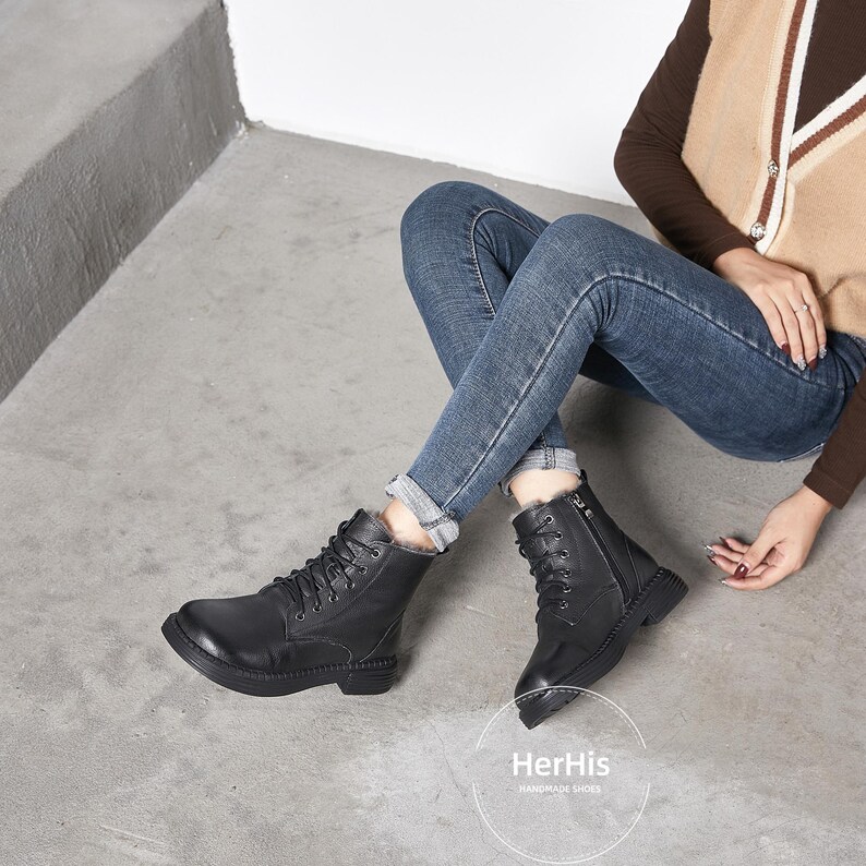 May include: Black leather ankle boots with laces and a zipper on the side. The boots have a thick sole and are worn by a person wearing jeans.
