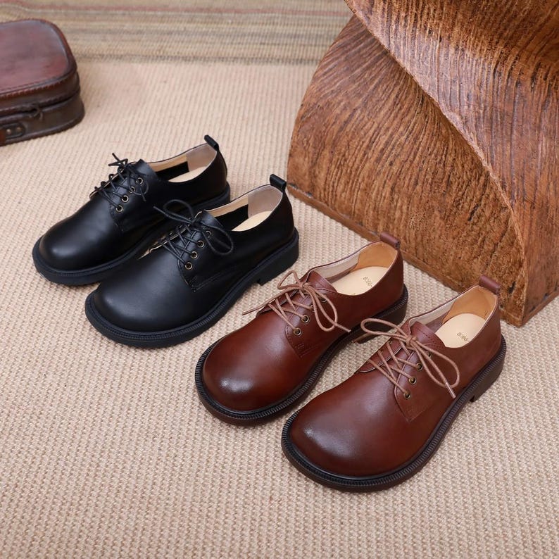 Puede incluir: Dos pares de zapatos de cuero con cordones. Un par es negro y el otro es marr&oacute;n.