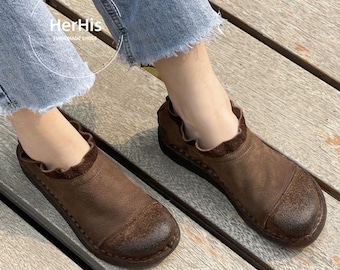 May include: Brown leather slip-on shoes with a rounded toe and a ruffled collar. The shoes are a warm brown color and appear to be handmade. The text "HerHis HANDMADE SHOES" is visible in the upper left corner.