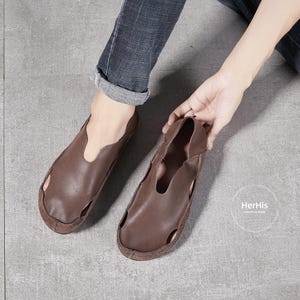 May include: A pair of brown leather slip-on shoes with a cut-out design. The shoes have a simple, casual style.