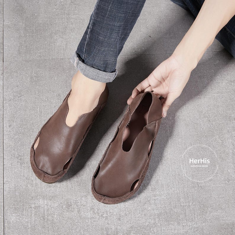 May include: A pair of brown leather slip-on shoes with a cut-out design. The shoes have a simple, casual style.