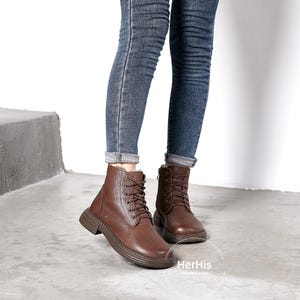 May include: Brown leather lace-up boots with a chunky sole. The boots are worn with blue jeans.