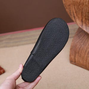 Op de afbeelding: Close-up van de zool van een zwarte leren schoen. De zool heeft een textuur, antislip ontwerp. De schoen wordt door een hand vastgehouden, die de details van het schoeisel laat zien. De schoen lijkt een loafer of een vergelijkbare stijl te zijn.