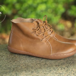 May include: Brown leather ankle boots with laces. The boots have a rounded toe and a slightly raised heel. The text "HerHis HANDMADE SHOES" is visible at the top of the image.