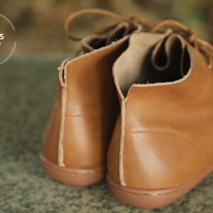 May include: A pair of brown leather ankle boots with laces. The boots have a rounded toe and a low heel. The brand name "HerHis Handmade Shoes" is visible on the left boot.