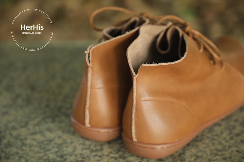 May include: A pair of brown leather ankle boots with laces. The boots have a rounded toe and a low heel. The brand name "HerHis Handmade Shoes" is visible on the left boot.