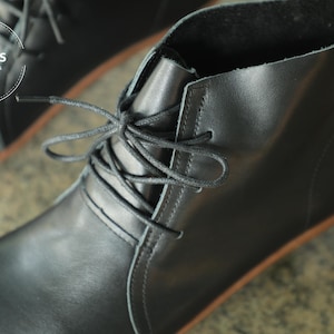May include: Black leather ankle boots with laces. The boots have a rounded toe and a low heel. The brand name "HerHis" is visible on the side of the boot.