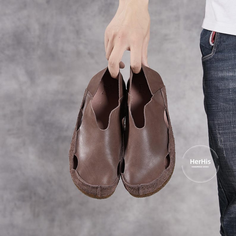 May include: A pair of brown leather slip-on shoes with a suede sole. The shoes have a simple design with a single strap across the top.