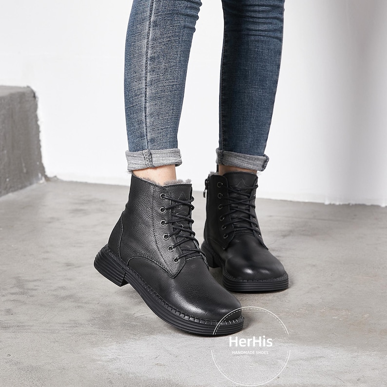 May include: Black leather ankle boots with a lace-up front and a zipper on the side. The boots have a thick sole and are lined with fur. The boots are worn by a person wearing jeans.