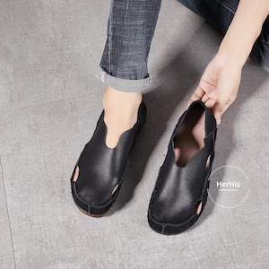 May include: A pair of black leather slip-on shoes with a unique open-toe design. The shoes have a simple, minimalist style and are made of soft, supple leather.