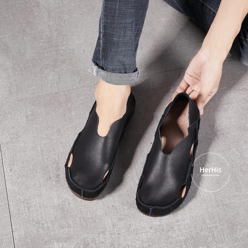 May include: A pair of black leather slip-on shoes with a unique open-toe design. The shoes have a simple, minimalist style and are made of soft, supple leather.