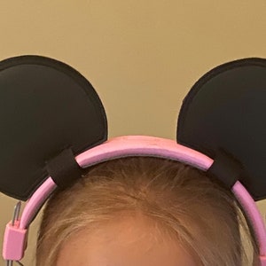 May include: Pink headband with black mouse ears. The headband is made of a soft, flexible material and is designed to fit comfortably on a child's head.