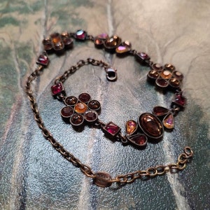 Puede incluir: Un collar de cadena dorada con un diseño floral con piedras rojas, naranjas e iridiscentes.