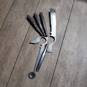 May include: A multi-tool with a silver finish and multiple blades. The tool has a long, thin handle and a variety of attachments, including a spoon, a knife, and a screwdriver.